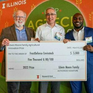 Three men smile and display a large check from the Edwin Moore Family for the 2022 Agricultural Innovation Prize, awarded to FrostDefense Envirotech for $5,000.
