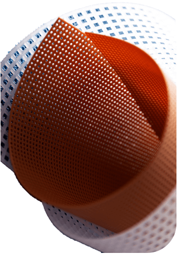 Close-up of layered, perforated materials. A curved, rust-orange sheet with small holes overlaps a flat, white sheet with a grid pattern of small squares. A third, barely visible sheet beneath also appears to have a grid pattern.